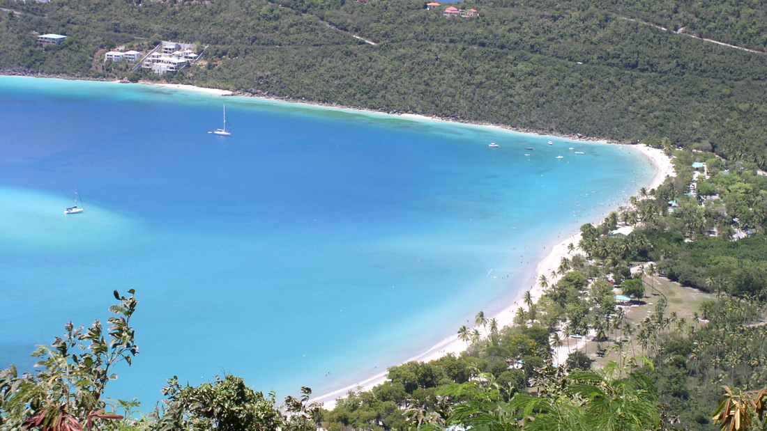 Magens Bay on St. Thomas, with turquoise water, a curving sandy beach, sailboats and green hills.