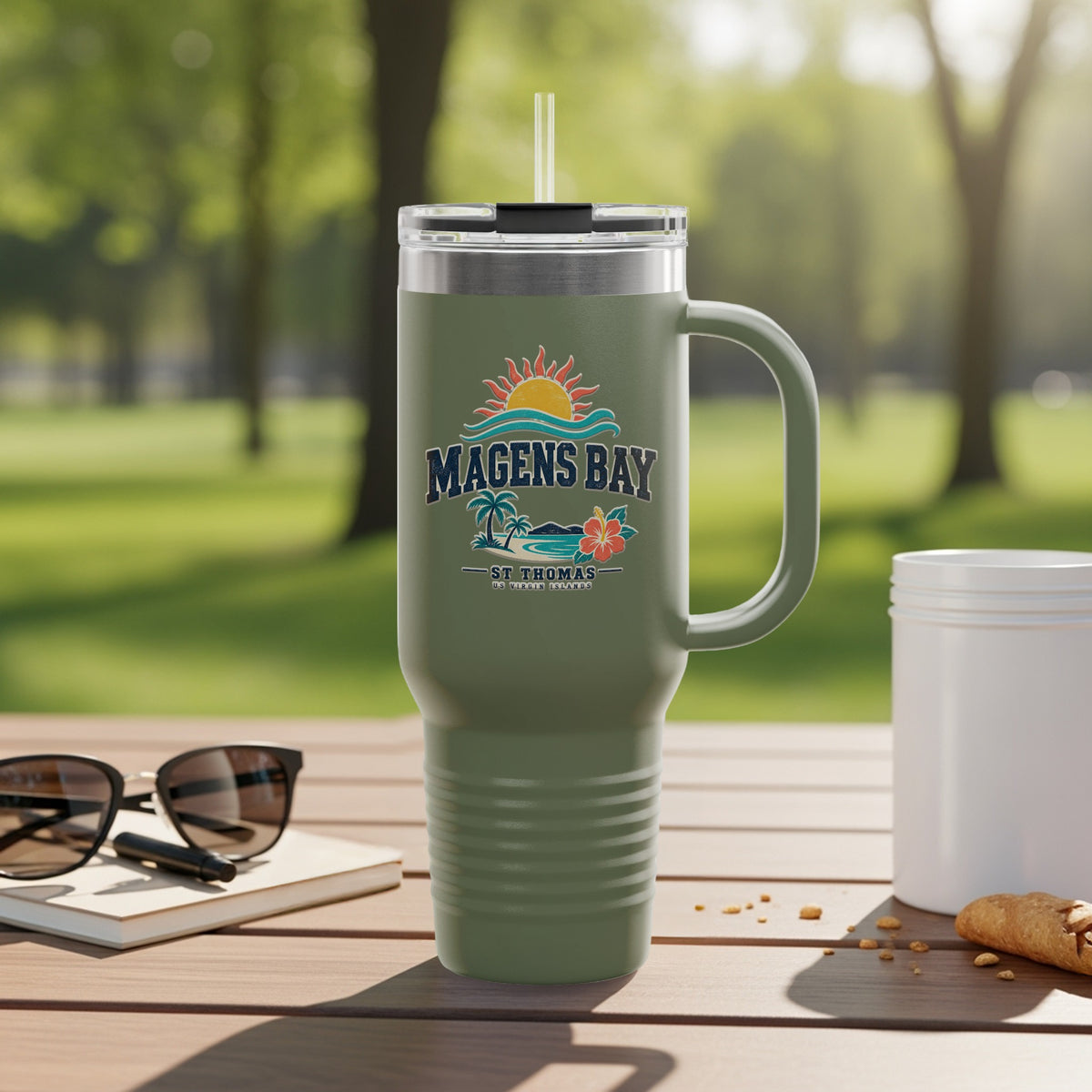 Green tumbler with Magens Bay, St. Thomas logo, set on a table outdoors.