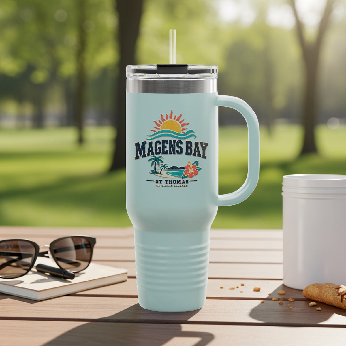 Light blue travel tumbler with Magens Bay St. Thomas logo outdoors.
