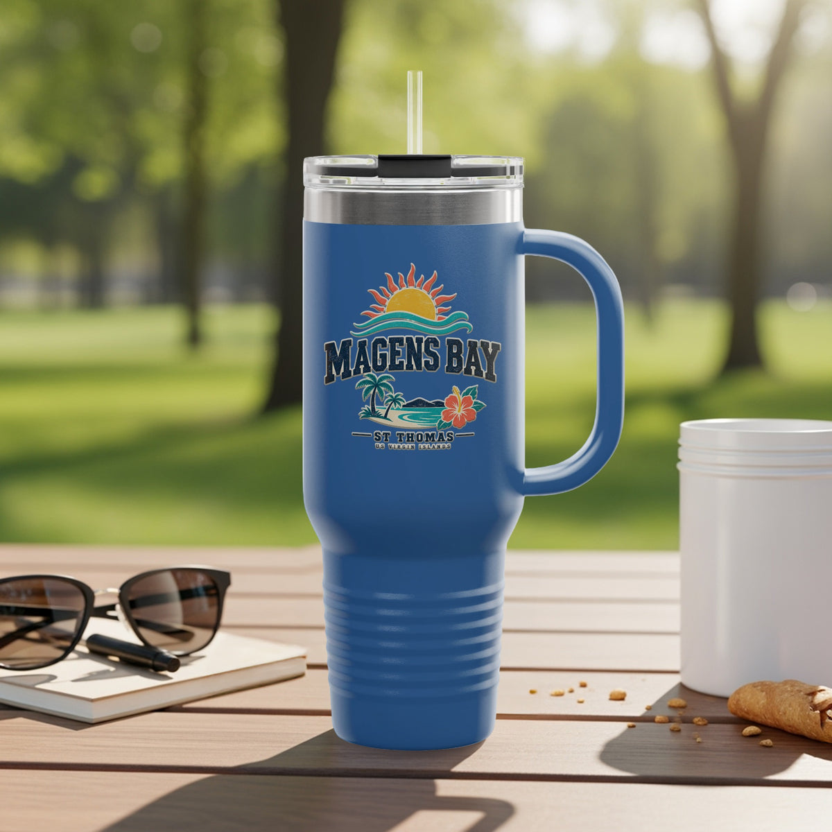 Blue tumbler with Magens Bay, St. Thomas logo on a wooden table.