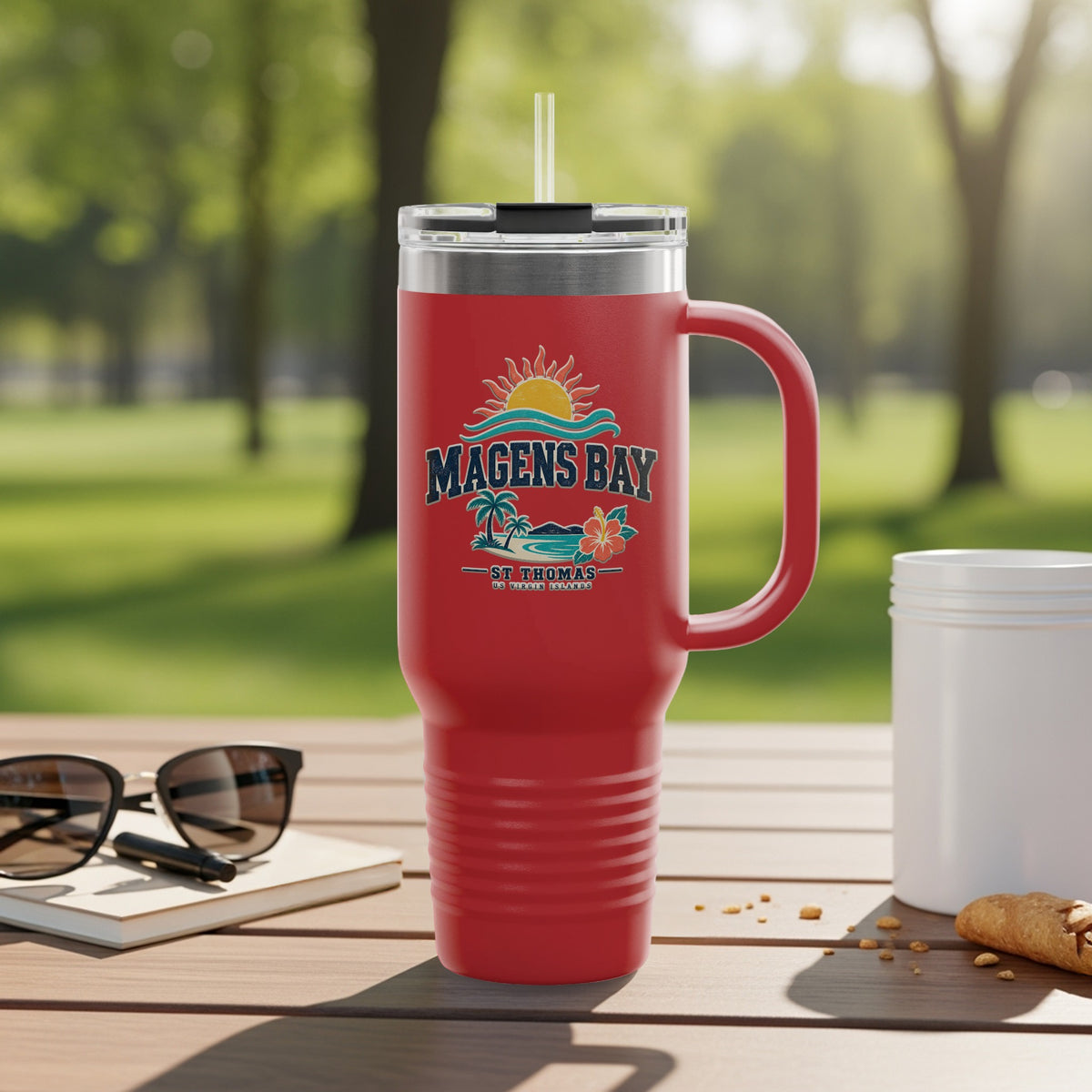 Red tumbler with Magens Bay St. Thomas graphic and straw outdoors.