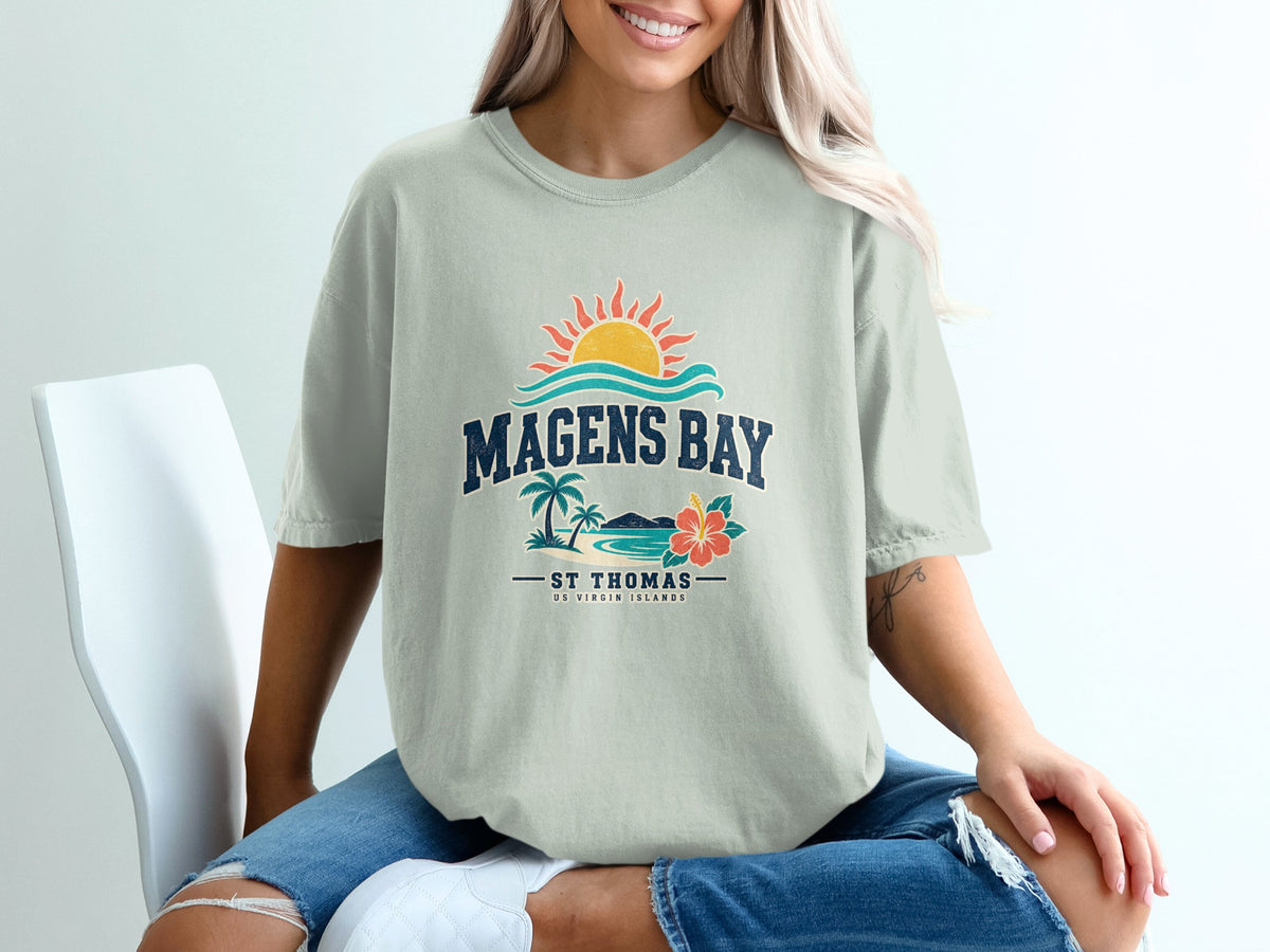 A person wearing a light gray t-shirt with a vintage-style graphic reading Magens Bay, St. Thomas, US Virgin Islands.