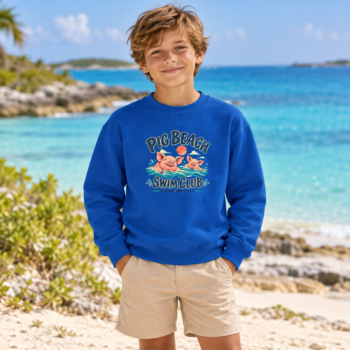 AI lifestyle mockup of a child wearing the royal blue Pig Beach Swim Club Exuma Bahamas Gildan 18000B youth sweatshirt on a tropical coast.